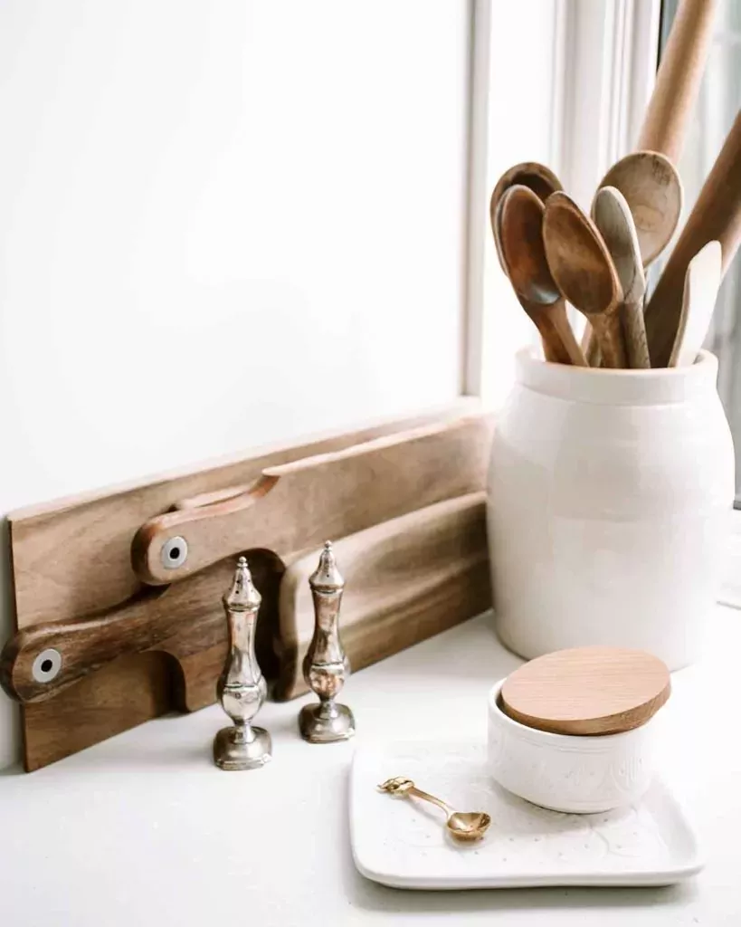 Wooden spoons and spatulas, in ceramic jar next to wooden cutting boards and some other stuff in a kitchen