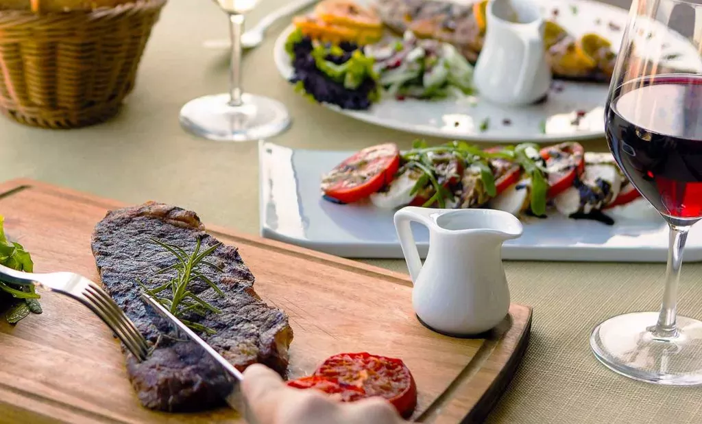 Cutting into a delicious flat iron steak on a cutting board, served with wine and an appetizer