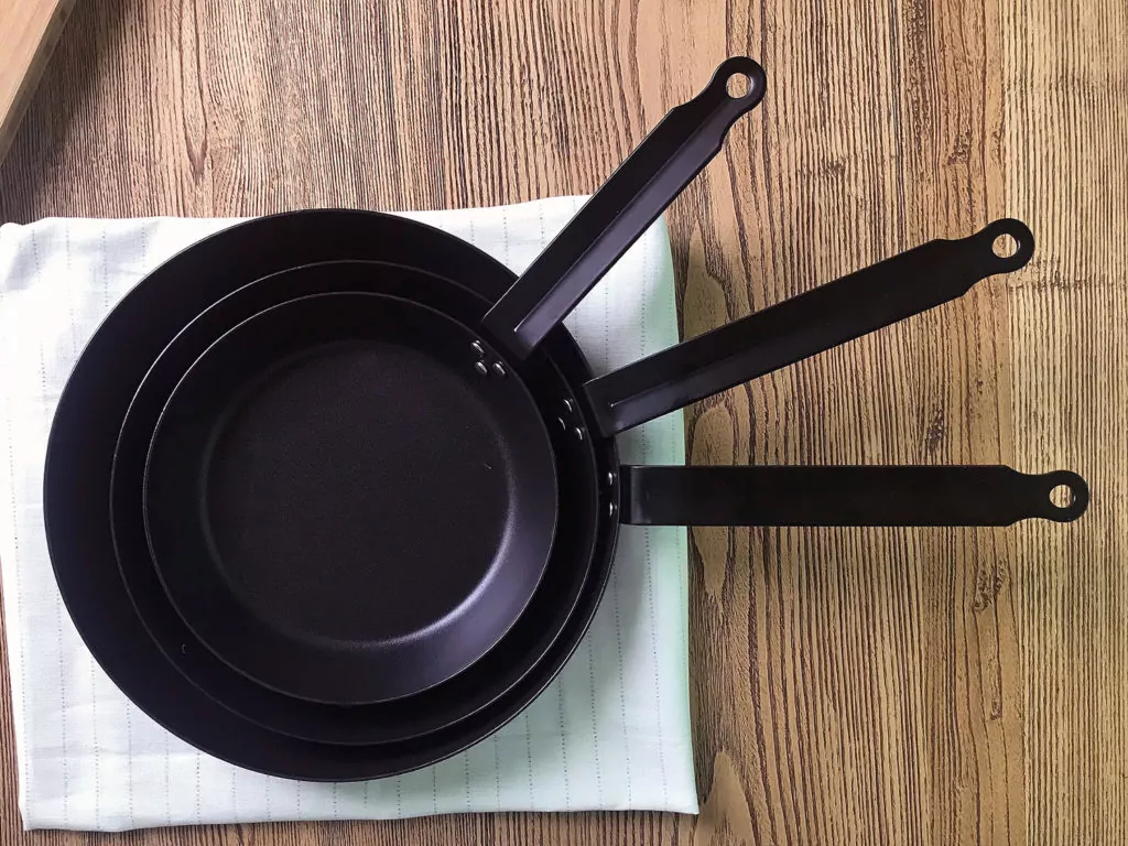 Three brand new carbon steel pans nested on a wood countertop