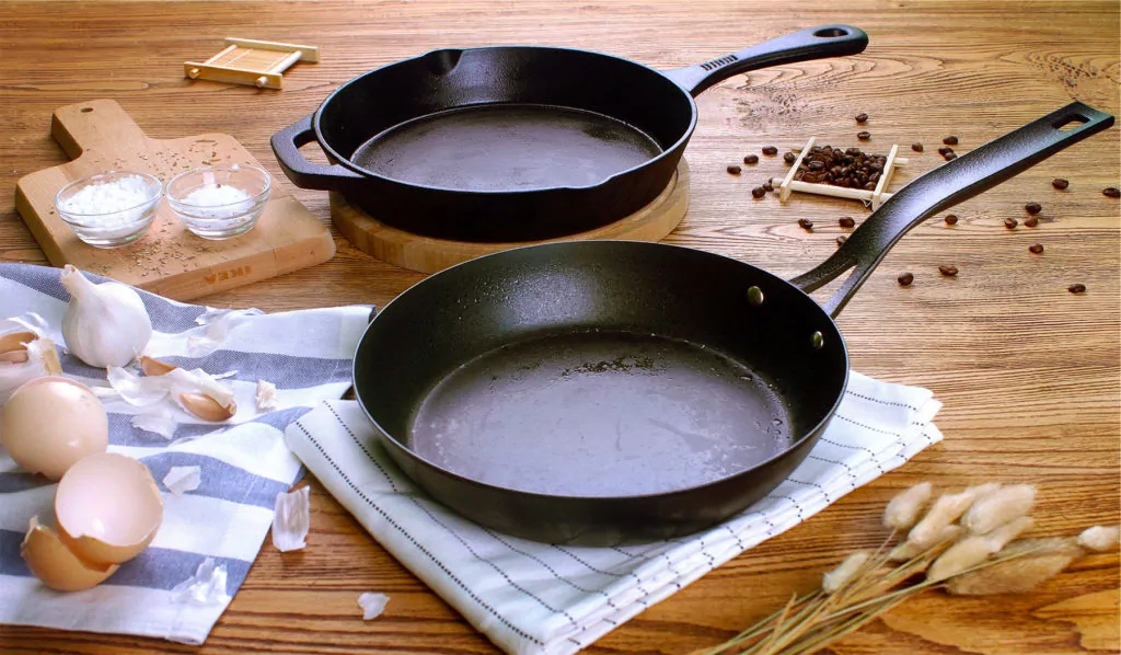 Cast Iron Pan behind a Carbon Steel Pan on kitchen counter with cooking ingredients scattered about