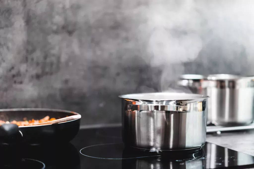 stainless steel pot cooking steaming on glass top electric stove with non-stick pan sauteing veggies to the left